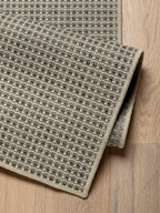 Detalle de alfombra de sisal arena con borde reforzado y textura tejida.