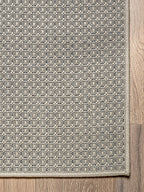 Vista esquina de alfombra de sisal marfil con borde perimetral tejido.