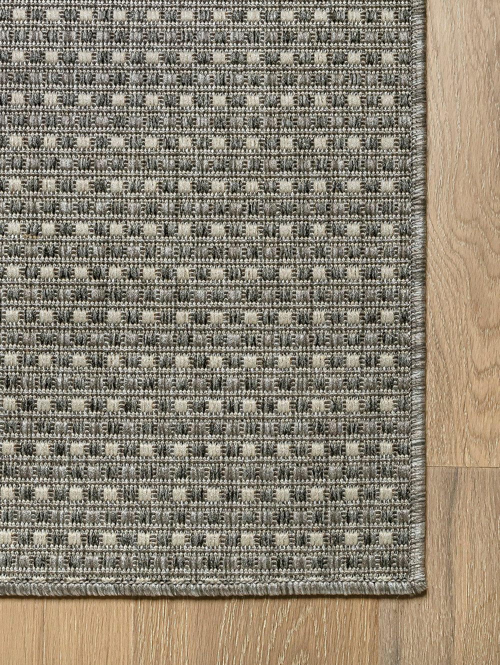 Vista de esquina de alfombra Sisalo Trilenium gris con borde perimetral tejido.