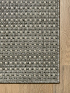 Vista de esquina de alfombra Sisalo Trilenium gris con borde perimetral tejido.